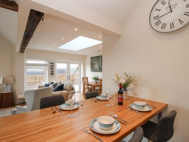 A dining table set with plates glasses and cutlery next to a living area with chairs sofa and a wooden dining table at Border View Lodge in Llandrinio