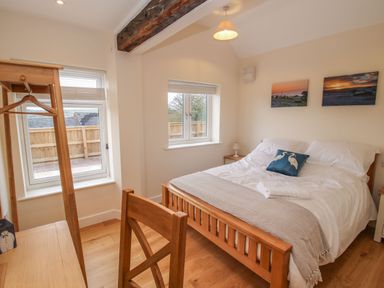 A bedroom with a wooden bed and chair and two windows at Border View Lodge in Llandrinio