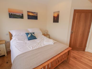 A bedroom with a wooden bed frame white bedding blue pillow and three landscape pictures on the wall at Border View Lodge in Llandrinio