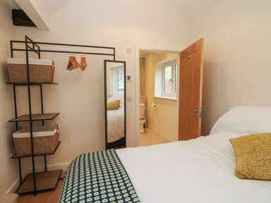 A bedroom with a bed and pillow a shelving unit with baskets and hangers and an open door leading to a bathroom at Border View Lodge in Llandrinio