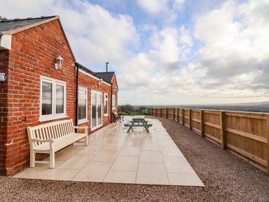 A brick house with white bench windows doors and wooden fence on tiled patio at Border View Lodge in Llandrinio