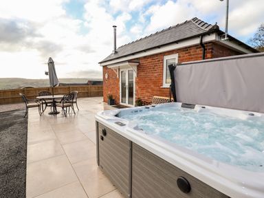 An outdoor patio with a hot tub and a table with four chairs and an umbrella at Border View Lodge in Llandrinio