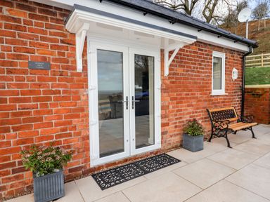 An exterior view of a brick building with white double doors a bench and two potted plants at Border View Lodge in Llandrinio