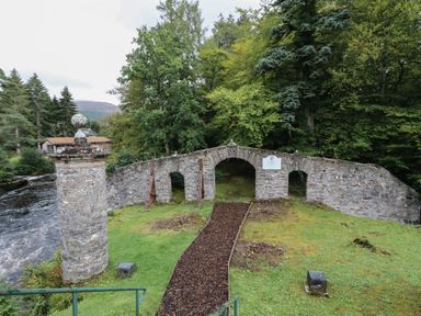 A stone bridge with three archways over a grassy area with trees in the background at Millmore Cabin in Killin