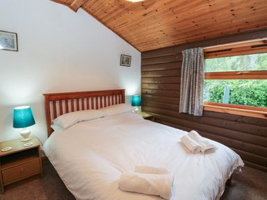 A bedroom with a double bed two bedside tables with lamps a window with curtains and wood paneling on the walls and ceiling at Millmore Cabin in Killin