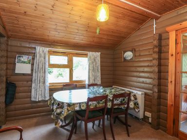 A dining area with a table and four chairs in a wooden cabin at Millmore Cabin in Killin