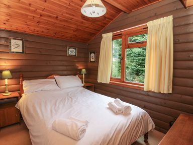 A bedroom with a double bed lit by two bedside lamps and a window with curtains at Millmore Cabin in Killin