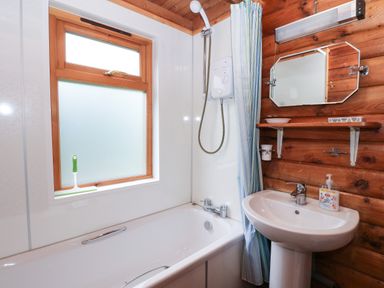A bathroom with a bathtub shower mirror sink and soap at Millmore Cabin in Killin