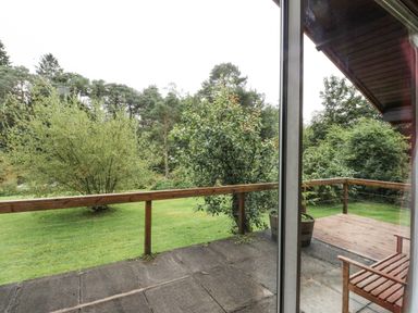 A patio with wooden railing and a bench overlooking a grassy yard with trees at Millmore Cabin in Killin
