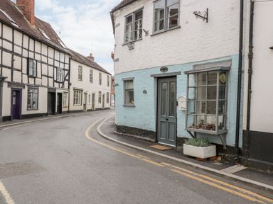 A street with old painted buildings including a blue and white house with a mailbox and a plant at Cobblers Cottage in Upton Upon Severn