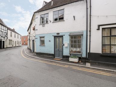 A street view of a cottage with a blue and white facade and a gray door at Cobblers Cottage in Upton Upon Severn