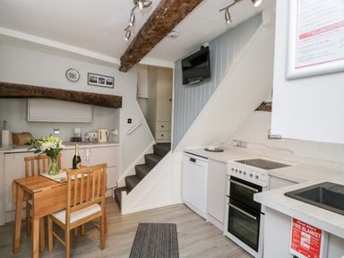 A kitchen with wooden dining table and chairs a built in oven dishwasher countertop sink and stairs at Cobblers Cottage in Upton Upon Severn