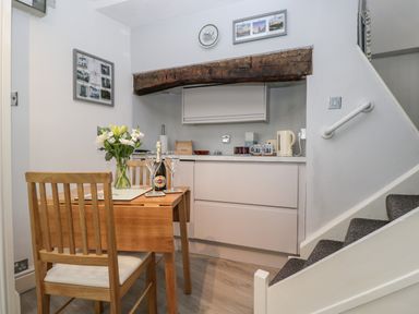 A small kitchen area with a wooden table and two chairs next to a staircase with a handrail at Cobblers Cottage in Upton Upon Severn