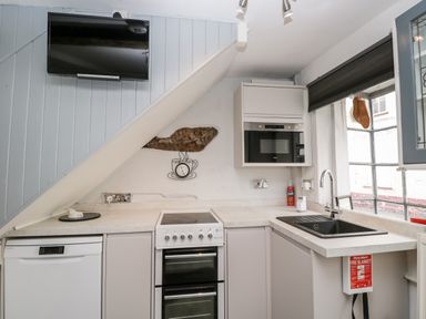 A kitchen with a stove dishwasher microwave sink and TV mounted on a slanted wall at Cobblers Cottage in Upton Upon Severn