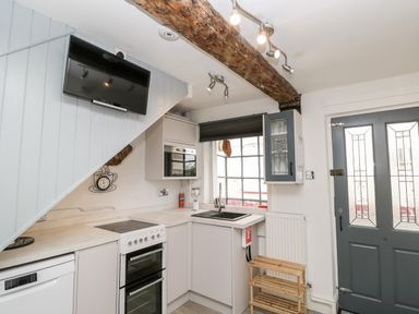 A kitchen with a stove dishwasher sink microwave wall mounted tv and wooden shelf at Cobblers Cottage in Upton Upon Severn