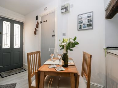 Dining area with wooden table and chairs a bottle and glasses on the table and grey front door at Cobblers Cottage in Upton Upon Severn