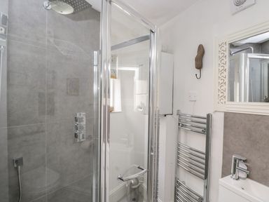 A bathroom with a glass shower enclosure a chrome towel rack a washbasin and a mirror at Cobblers Cottage in Upton Upon Severn