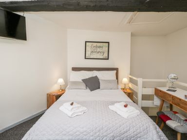 A bedroom with a double bed bedside tables lamps a wall-mounted TV and a wooden dressing table at Cobblers Cottage in Upton Upon Severn