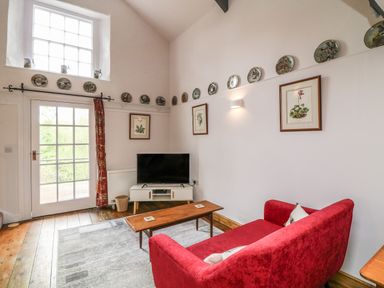 A sitting room with a red sofa wooden coffee table TV on a stand decorative plates on the walls at Wisteria Cottage in Marldon