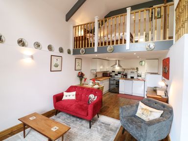 A living room with red and grey armchairs a wooden coffee table and an open kitchen with wood floors at Wisteria Cottage in Marldon