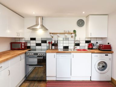A kitchen with white cabinets wooden countertops and black white and gray tiled backsplash at Wisteria Cottage in Marldon