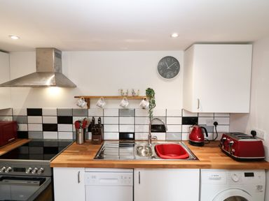 A kitchen with a stove hood dishwasher washing machine sink and red appliances at Wisteria Cottage in Marldon