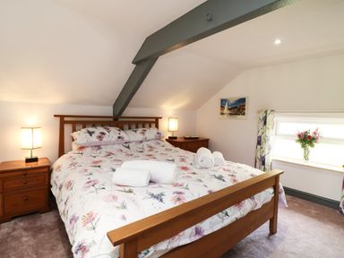 A bedroom with a wooden bed with floral bedding two bedside tables with lamps a window with floral curtains and a vase of flowers at Wisteria Cottage in Marldon