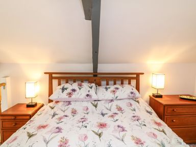A bedroom with a double wooden bed with floral bedding and two wooden bedside tables with lamps at Wisteria Cottage in Marldon