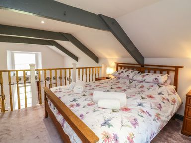 A bedroom with a wooden bed frame and floral bedding under exposed ceiling beams at Wisteria Cottage in Marldon
