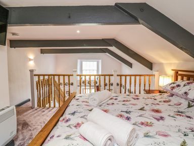 A loft bedroom with a floral bedspread rolled towels wooden railings and exposed ceiling beams at Wisteria Cottage in Marldon