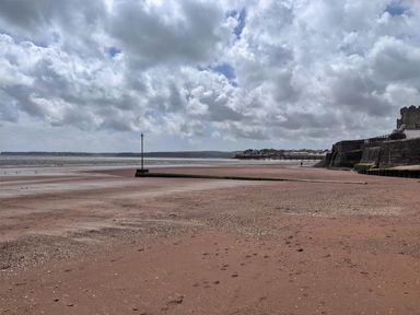 A sandy beach with footprints a seawall and sky with clouds at Wisteria Cottage in Marldon