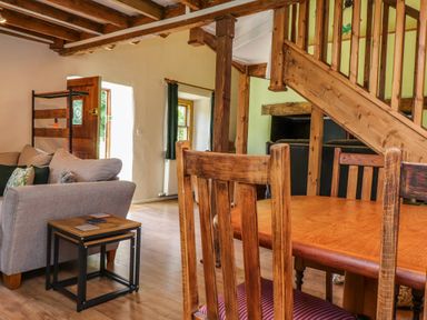 A living room with wooden dining chairs a wooden table a gray sofa a small wooden side table and wooden stairs at Bwthyn Gwyn Ty'n Y Pant in Boduan near Nefyn
