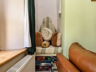 A corner seating area with cushions and board games below near a brown leather sofa at Bwthyn Gwyn Ty'n Y Pant in Boduan near Nefyn