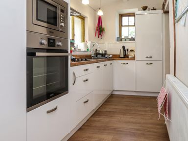 A kitchen with white cabinets, built-in oven and microwave, wooden countertop, sink under a window, kettle, and coffee maker at Bwthyn Gwyn Ty'n Y Pant in Boduan near Nefyn