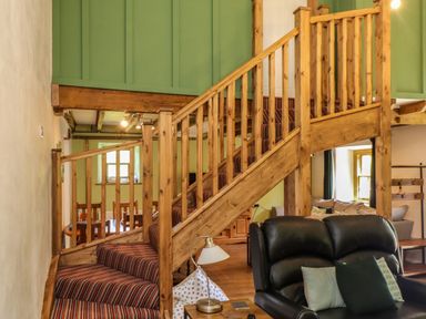 A wooden staircase with striped carpet and a black leather chair with cushions in a living area at Bwthyn Gwyn Ty'n Y Pant in Boduan near Nefyn