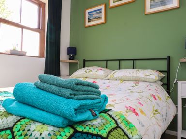 A bedroom with a bed with floral bedding a stack of green and blue towels and framed pictures on a green wall at Bwthyn Gwyn Ty'n Y Pant in Boduan near Nefyn