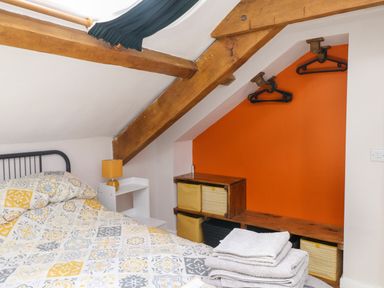 A bedroom with a bed covered in patterned bedding next to a small nightstand with a lamp and shelving with yellow storage bins at Bwthyn Gwyn Ty'n Y Pant in Boduan near Nefyn