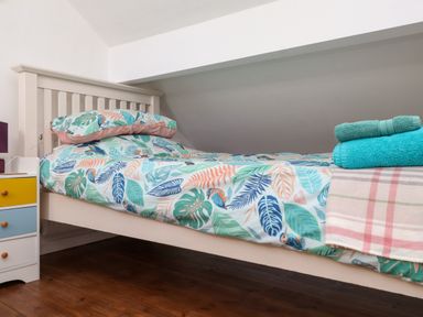 A single bed with leaf patterned bedding and towels on top next to a small chest of drawers at Bwthyn Gwyn Ty'n Y Pant in Boduan near Nefyn