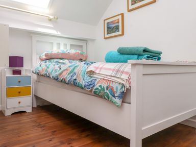 A bedroom with a white wooden bed colorful bedding folded towels and a nightstand with a purple lamp at Bwthyn Gwyn Ty'n Y Pant in Boduan near Nefyn