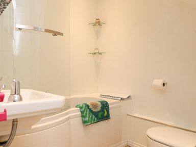 A bathroom with a bathtub a sink a toilet a towel on the bathtub and two glass shelves with containers at Bwthyn Gwyn Ty'n Y Pant Boduan near Nefyn