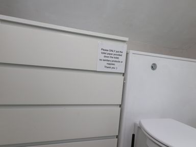 A bathroom with a white toilet and a white cabinet with a sign about toilet paper at Bwthyn Gwyn Ty'n Y Pant in Boduan near Nefyn