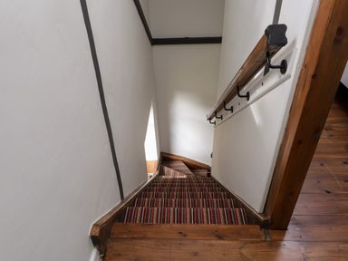A staircase with striped carpet and wooden handrail leading down from a wooden floor at Bwthyn Gwyn Ty'n Y Pant in Boduan near Nefyn