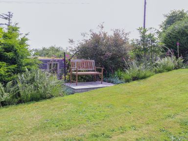 A garden with a wooden bench on a raised platform surrounded by bushes and flowers at Bwthyn Gwyn Ty'n Y Pant in Boduan near Nefyn