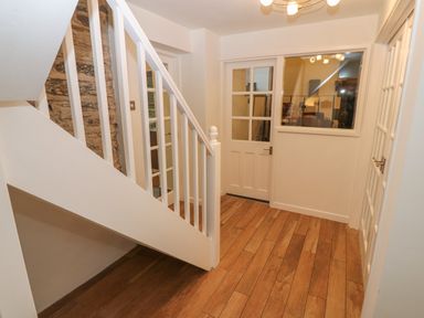 A hallway with wooden flooring white staircase and doors with glass panels at Yr Hen Ysgol The Old School Prenteg