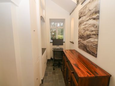A narrow room with a wooden sideboard a computer on a desk and a large abstract painting on the wall at Yr Hen Ysgol The Old School in Prenteg
