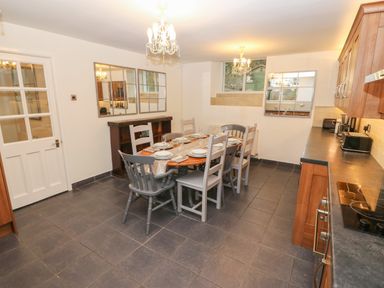 A kitchen dining area with a table set for six chairs and wooden cabinets at Yr Hen Ysgol The Old School in Prenteg