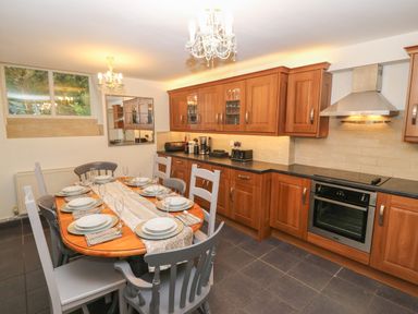 A kitchen with wooden cabinets a dining table set with plates and glasses at Yr Hen Ysgol The Old School in Prenteg