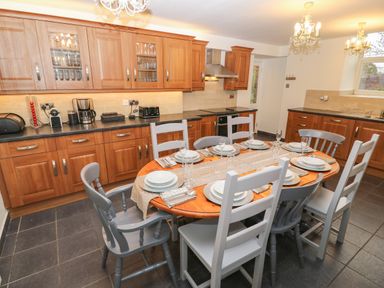 A kitchen with wooden cabinets a dining table set with plates and glasses at Yr Hen Ysgol The Old School in Prenteg