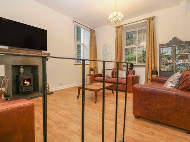 A sitting room with brown leather sofas a coffee table a fireplace with a wood stove and a television above at Yr Hen Ysgol The Old School in Prenteg