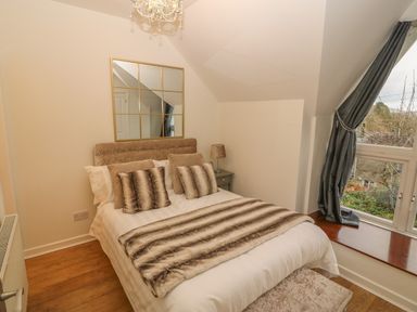 A bedroom with a bed next to a window with curtains and a chandelier at Yr Hen Ysgol The Old School in Prenteg